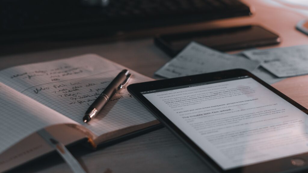 A warm-toned desk setup featuring a tablet, notebook, and pen for a productive workspace.